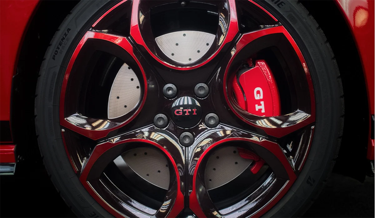 Nahaufnahme einer schwarzen GTI Felge mit Radschraubenkappen, GTI Nabenkappe und rotem Bremssattel.