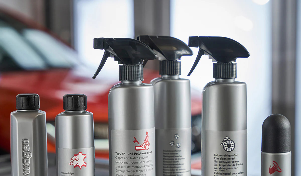Autopflege-Reinigungsprodukte in silbernen Sprühflaschen für Leder, Teppich, Polster und Felgen vor einem Fahrzeug