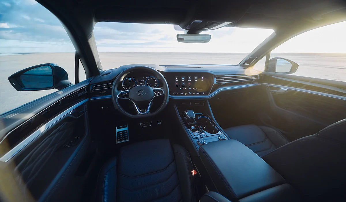 Innenraum eines Volkswagen Fahrzeugs mit Lenkrad, digitalem Cockpit, Mittelkonsole und Blick durch die Frontscheibe auf eine helle Landschaft.