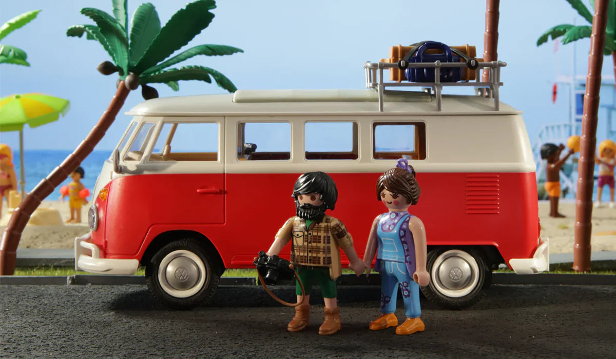 Playmobil Figuren vor rotem Volkswagen Bulli Modellauto am Strand mit Palmen