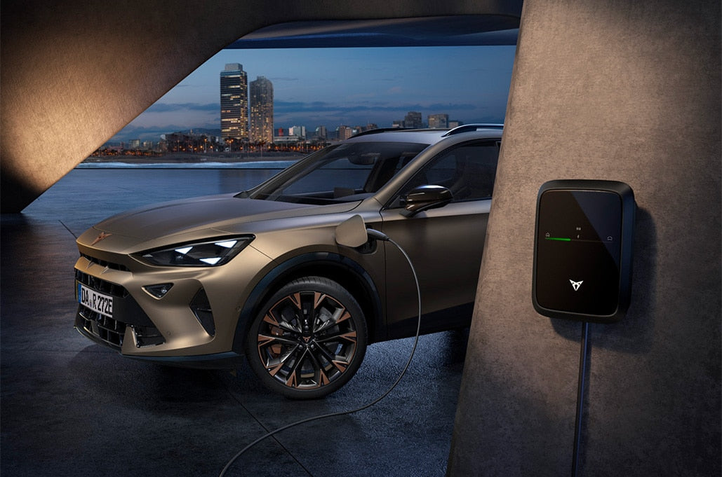 Bronzefarbener CUPRA lädt abends an der CUPRA Charger Pro 2 Wallbox vor Stadtkulisse