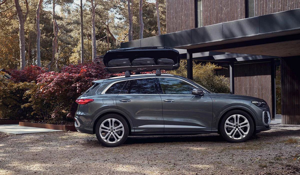 Audi SUV mit Dachbox und Gepäcktaschen vor modernem Haus im Grünen