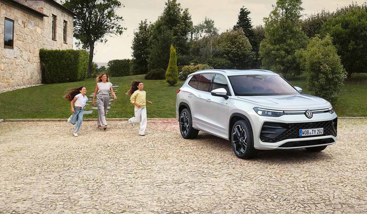 Weißer Volkswagen SUV vor modernem Landhaus mit Familie auf gepflastertem Hof